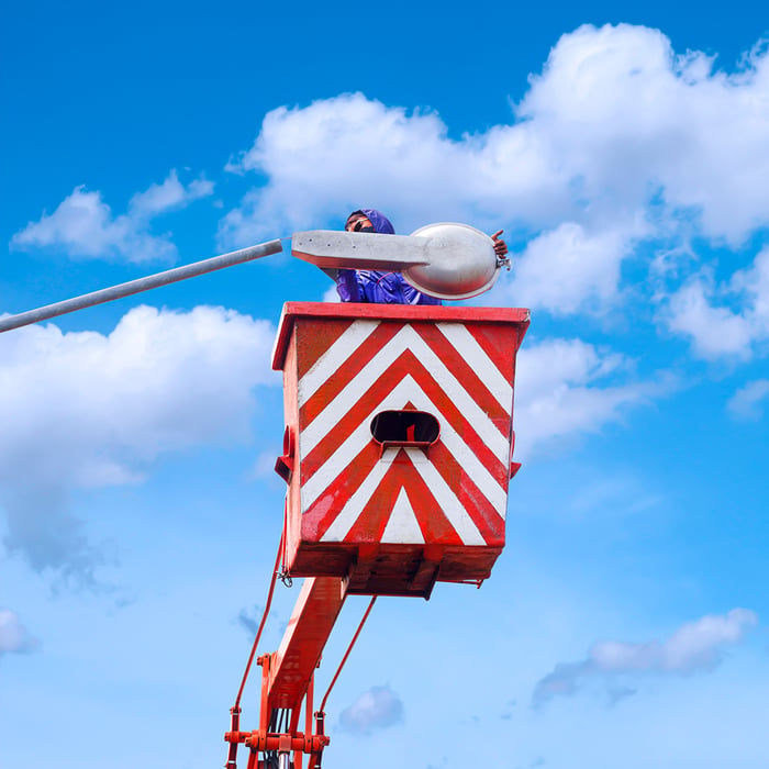 A man operating a crane against a blue sky backdrop, overseeing the installation of smart street lighting.