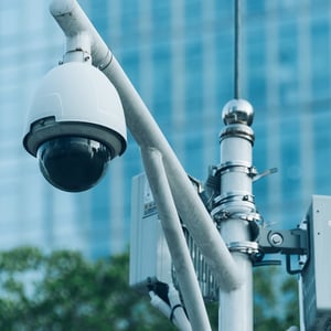 A pole-mounted camera in front of a building moniotring traffic.