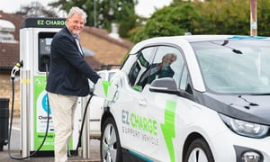 A man plugs a charging cable into an EZ-Charge electric support vehicle at an EZ-Charge public station.