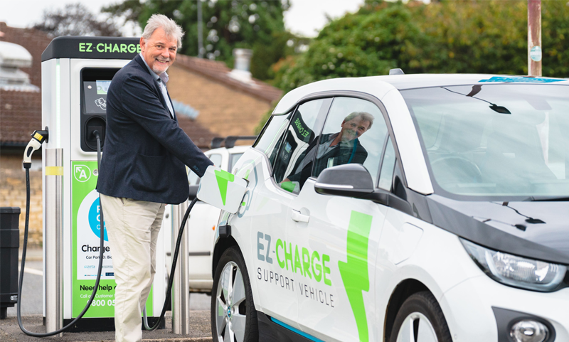 A man plugs a charging cable into an EZ-Charge electric support vehicle at an EZ-Charge public station.