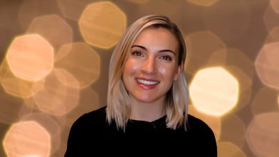 Portrait of a blonde woman in a black shirt against a background of blurred golden bokeh lights.