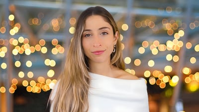 Portrait of a woman with long blonde hair wearing a white top against a background of blurred golden lights.