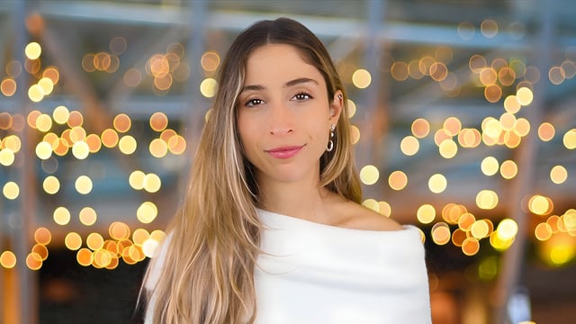 Portrait of a woman with long blonde hair wearing a white top against a background of blurred golden lights.
