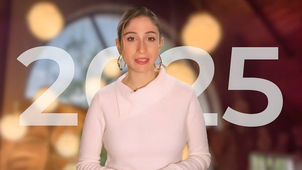 A woman in a white sweater speaking with the year 2025 overlaid in large white text against a blurred indoor background.