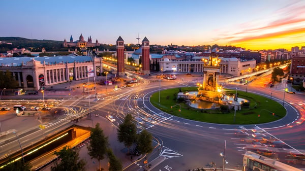 Long exposure aerial view of Plaça d'Espanya in Barcelona at sunset with light trails from traffic around the fountain.