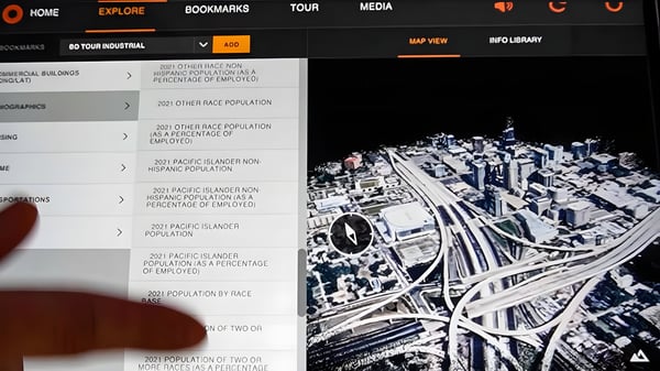 A finger points to a digital twin interface displaying a 3D map of city skyscrapers and highway interchanges.