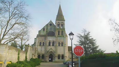 Stone church with a tall spire and rose window in a French village featuring a red stop sign and black street lamp.