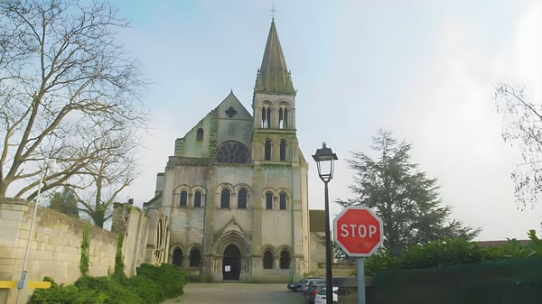Stone church with a tall spire and rose window in a French village featuring a red stop sign and black street lamp.