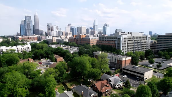 Aerial view of the Charlotte, North Carolina skyline behind a foreground of green trees and residential buildings.