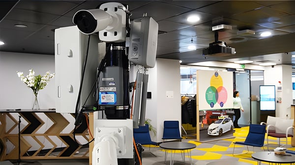 A mounted Sony camera and sensors in an office with a ServCity project poster featuring a Nissan autonomous vehicle.