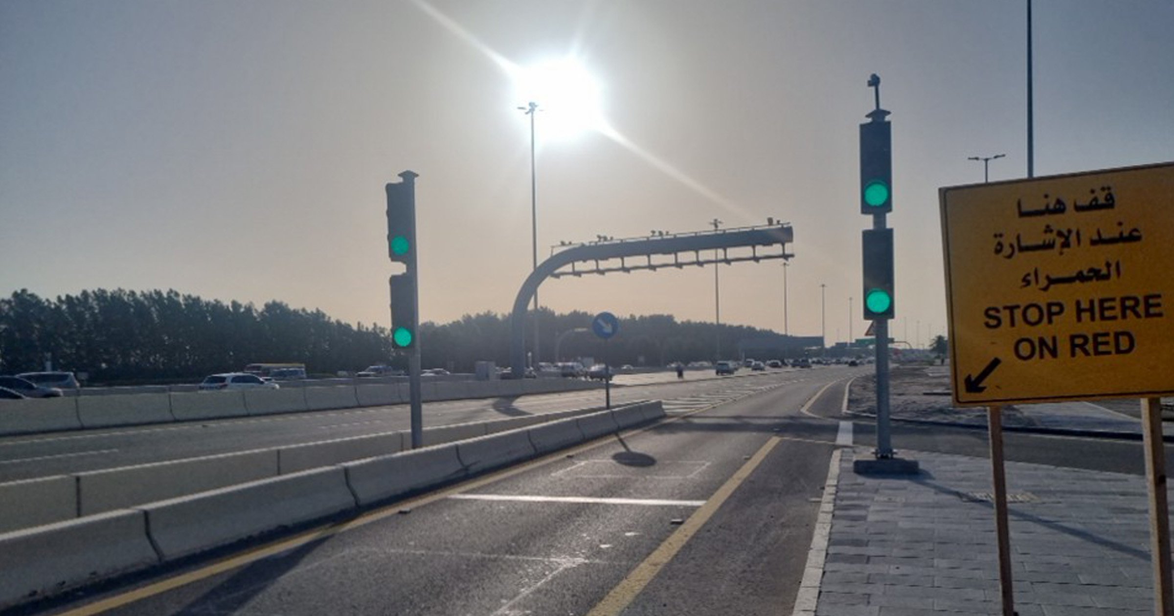 Green ramp meter lights and a yellow "Stop Here On Red" sign in Arabic and English on an Abu Dhabi highway.