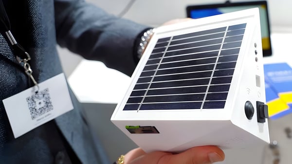 A person holding a white solar-powered air quality sensor at a trade show.