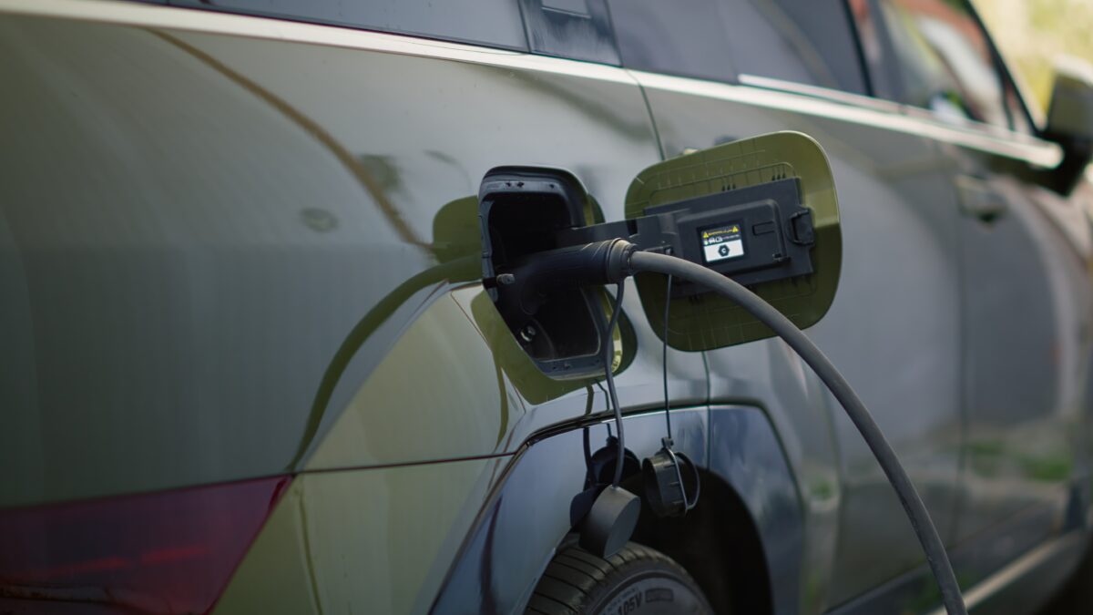 Close-up of a dark-colored electric vehicle charging, with a black charging cable plugged into its rear port.