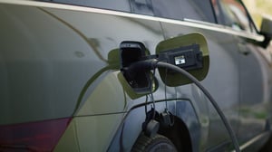 Close-up of a dark-colored electric vehicle charging, with a black charging cable plugged into its rear port.