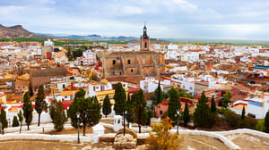 Elevated view of a historic Spanish town with a central stone church, terracotta-roofed buildings, and distant hills