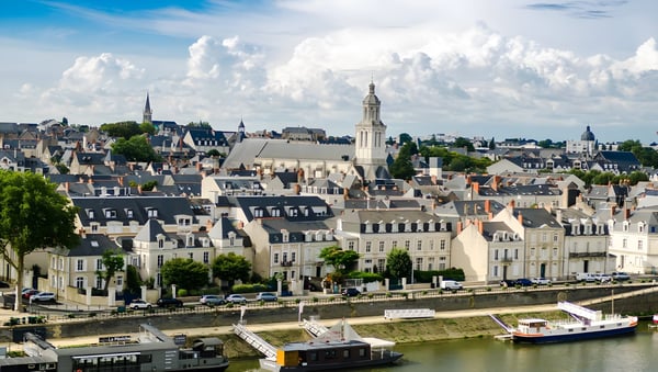 Skyline of Angers, France, featuring historic stone buildings and the Maine River with docked boats.