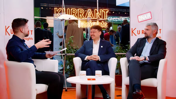 Three men in suits sit in white armchairs for a Kurrant Insights interview at a trade show booth with neon signage.