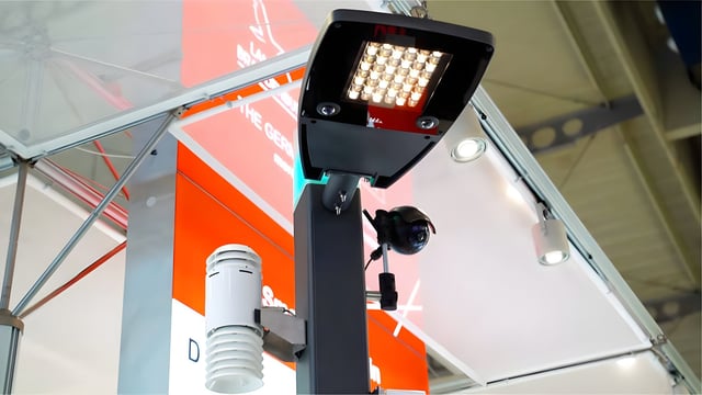 A smart street pole equipped with an LED luminaire, a security camera, and an environmental sensor at a trade show booth.