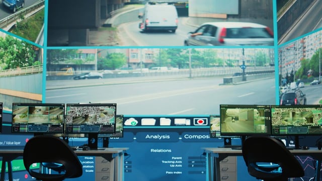 Empty operations room with a large wall screen showing road traffic camera feeds above desks with monitors and mapping software