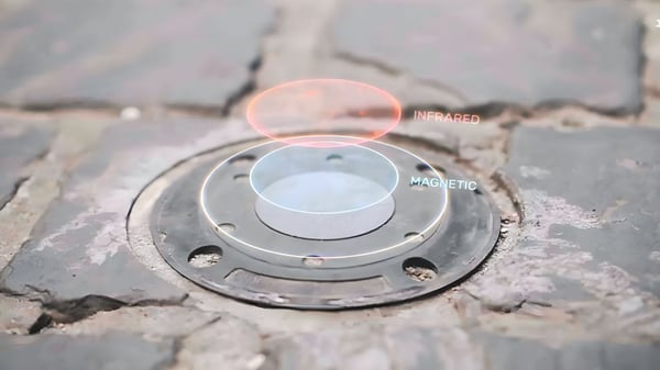 A circular smart parking sensor embedded in a cobblestone street with infrared and magnetic data overlays.
