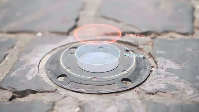 A circular smart parking sensor embedded in a cobblestone street with infrared and magnetic data overlays.