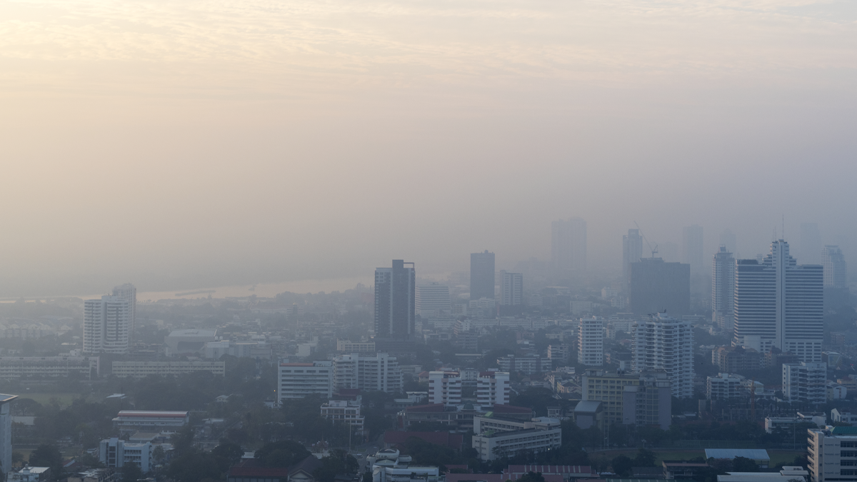 Hazy high-angle view of a city skyline obscured by thick smog and air pollution under a pale sky