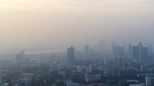 Hazy high-angle view of a city skyline obscured by thick smog and air pollution under a pale sky