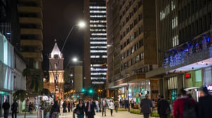 Nighttime street view of a bustling city street with pedestrians, modern high-rise buildings, and illuminated streetlights.