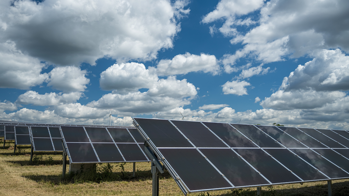 Rows of solar panels in a field under a blue sky with fluffy white clouds