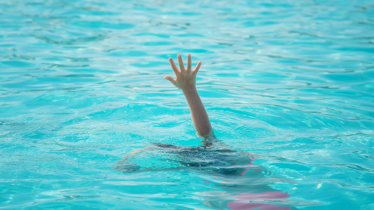 A hand reaching out above bright blue swimming pool water with a person submerged beneath the surface.