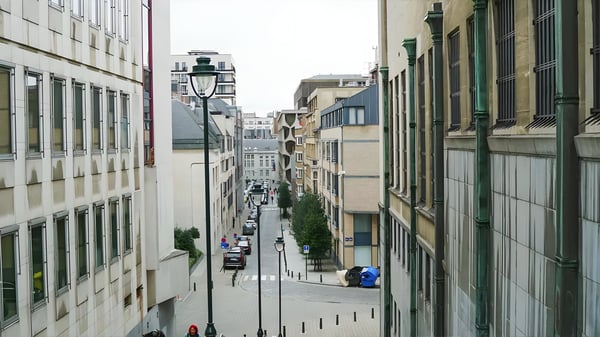 A narrow Brussels street viewed from an elevated position featuring traditional black lamp posts and parked cars.