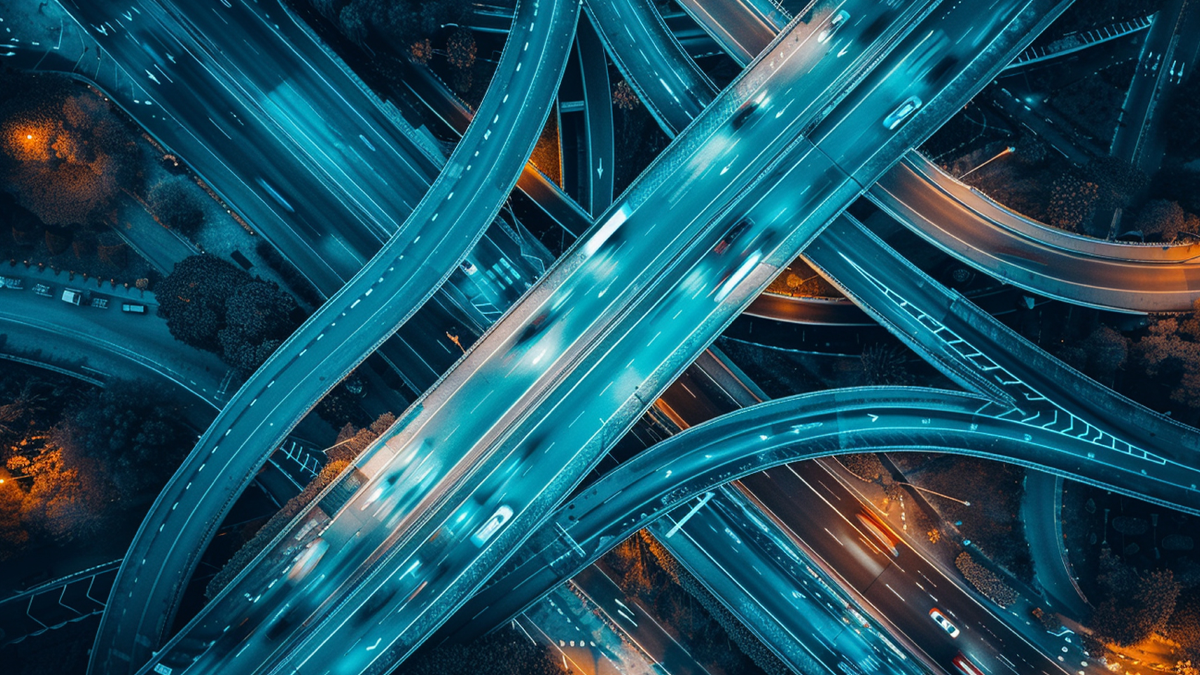 Aerial top-down view of a complex highway interchange at night with glowing blue and orange vehicle light trails