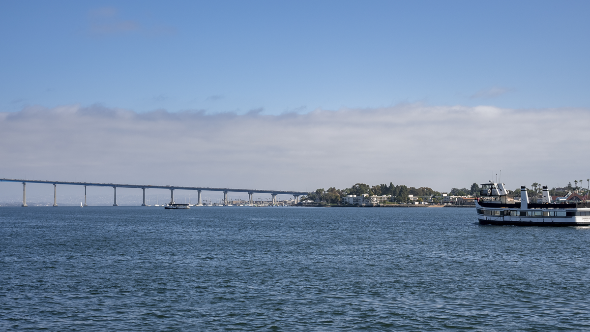 San Diego-Coronado Bridge spanning across a bay with boats sailing under a partly cloudy sky.