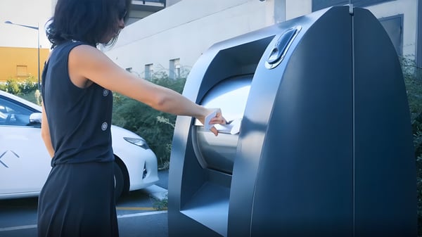 Woman using a keycard to unlock a modern smart waste bin with access control on a city street.