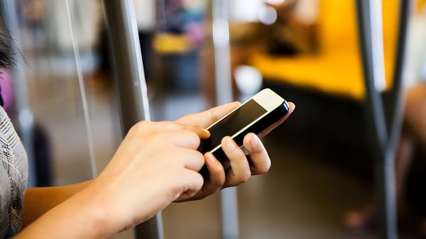 Close-up of a person's hands using a smartphone while standing on a public transit bus or train.