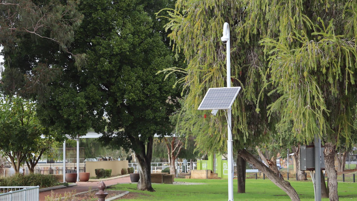 A solar-powered camera mounted on a white pole in a grassy park with trees in Yokine, City of Stirling
