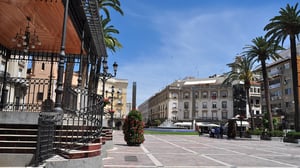 Sunny public plaza in Huelva featuring an ornate bandstand, street lights, palm trees, and surrounding buildings.
