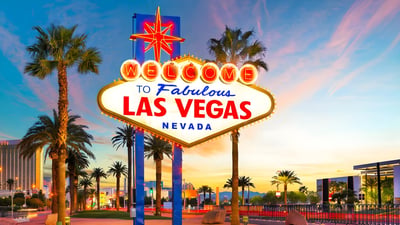 The Welcome to Fabulous Las Vegas sign stands at sunset surrounded by palm trees and city infrastructure.