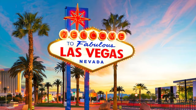 The Welcome to Fabulous Las Vegas sign stands at sunset surrounded by palm trees and city infrastructure.