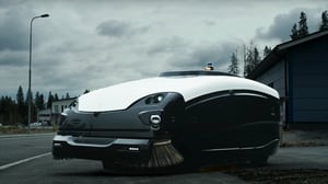A Trombia Technologies autonomous electric street sweeper with sweeping brushes parked on asphalt under cloudy skies.