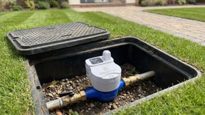 A white and blue smart water meter installed in an open underground utility box in a grassy lawn.
