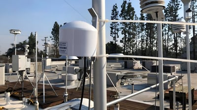 PurpleAir PA-II air quality sensor zip-tied to a metal pole on a rooftop monitoring station with other meteorological gear.