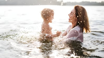 A woman and a young child splashing in a sunlit river or lake during the day.