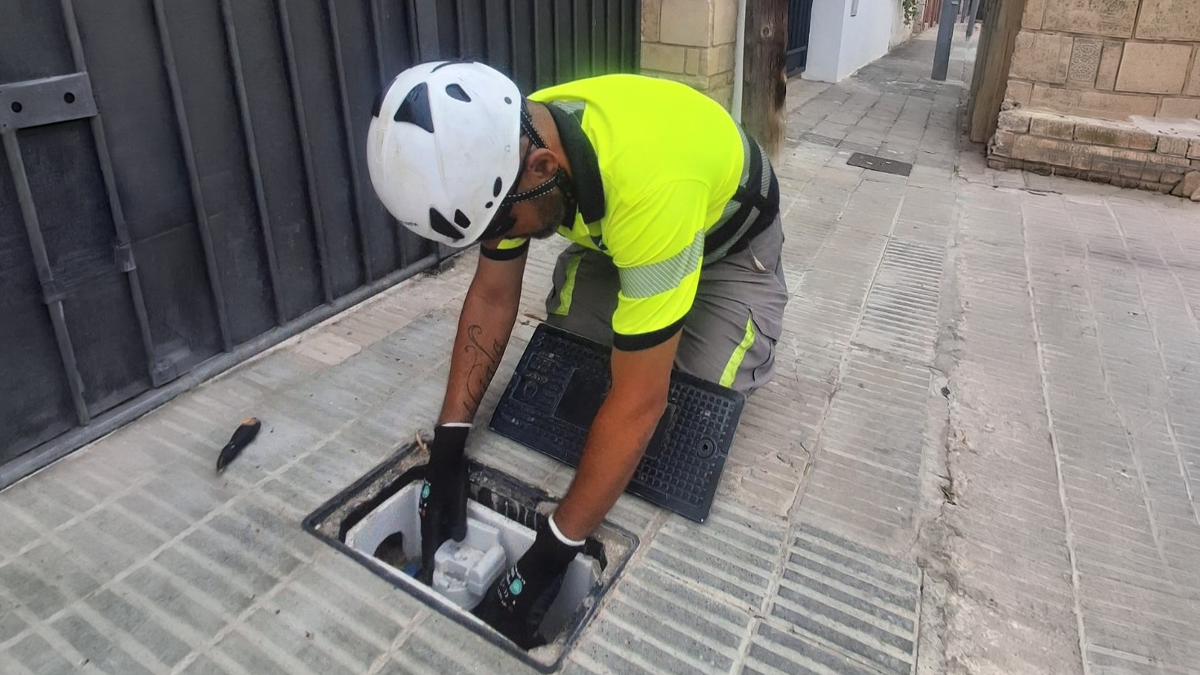 A utility worker in a high-visibility shirt and helmet installs a smart water meter in an underground street hatch.