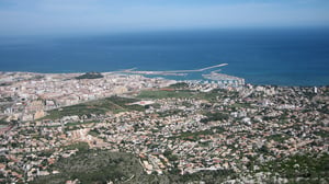 Aerial view of coastal Dénia showing buildings, a harbor, breakwater, and the Mediterranean Sea.