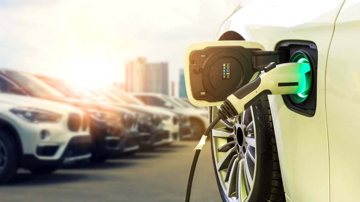Close-up of an electric vehicle charging at a station with a row of parked cars and a city skyline in the background