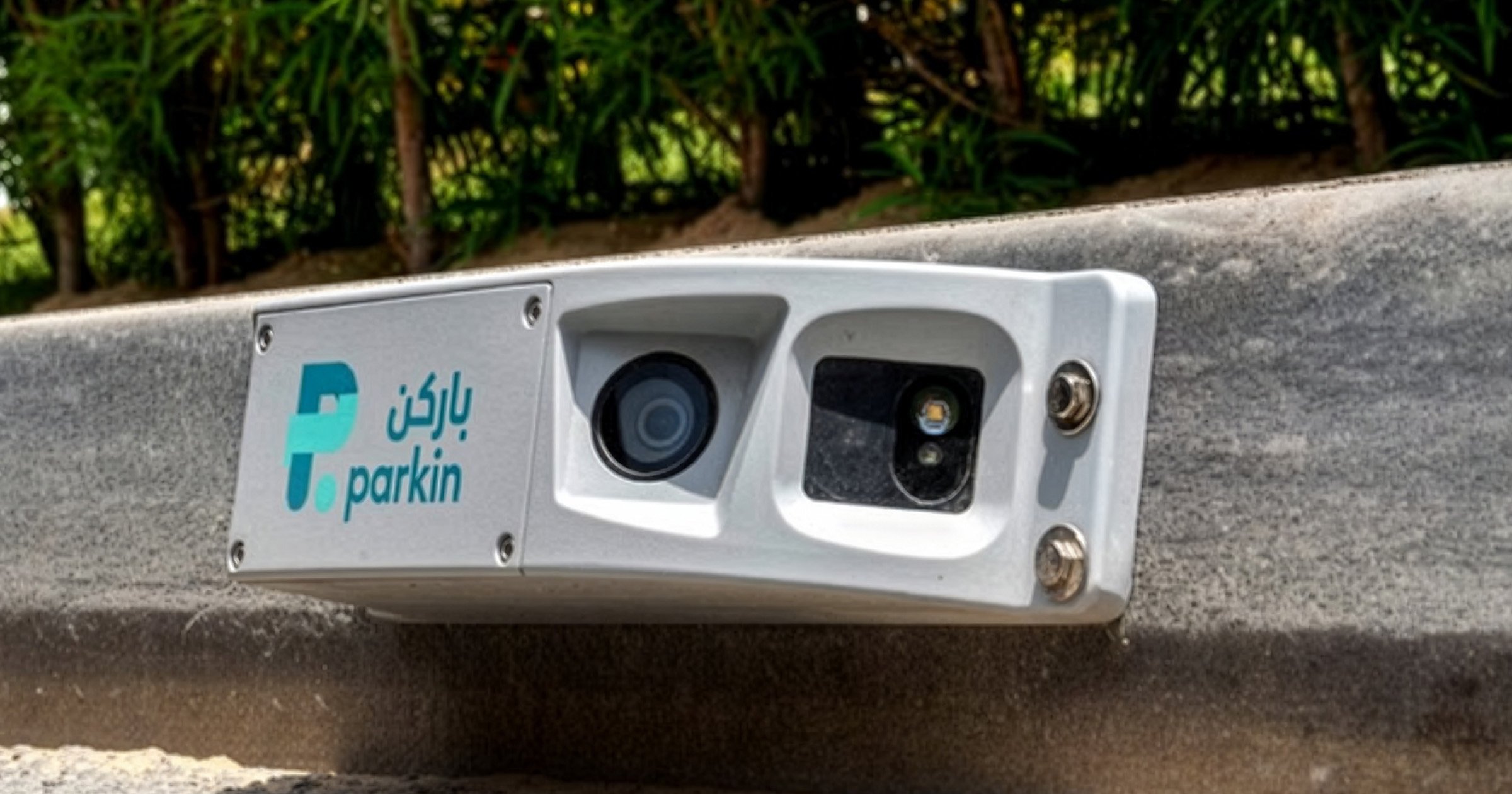 A Parkin Company branded AI parking camera mounted on a concrete curb in an outdoor setting.