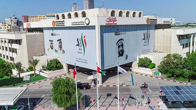 Aerial view of the DEWA headquarters building in Dubai featuring large banners of UAE leaders and national flags