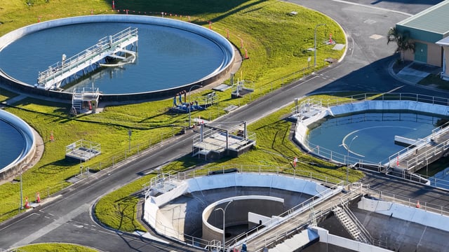 Aerial view of circular water treatment tanks and clarifier basins surrounded by green grass.