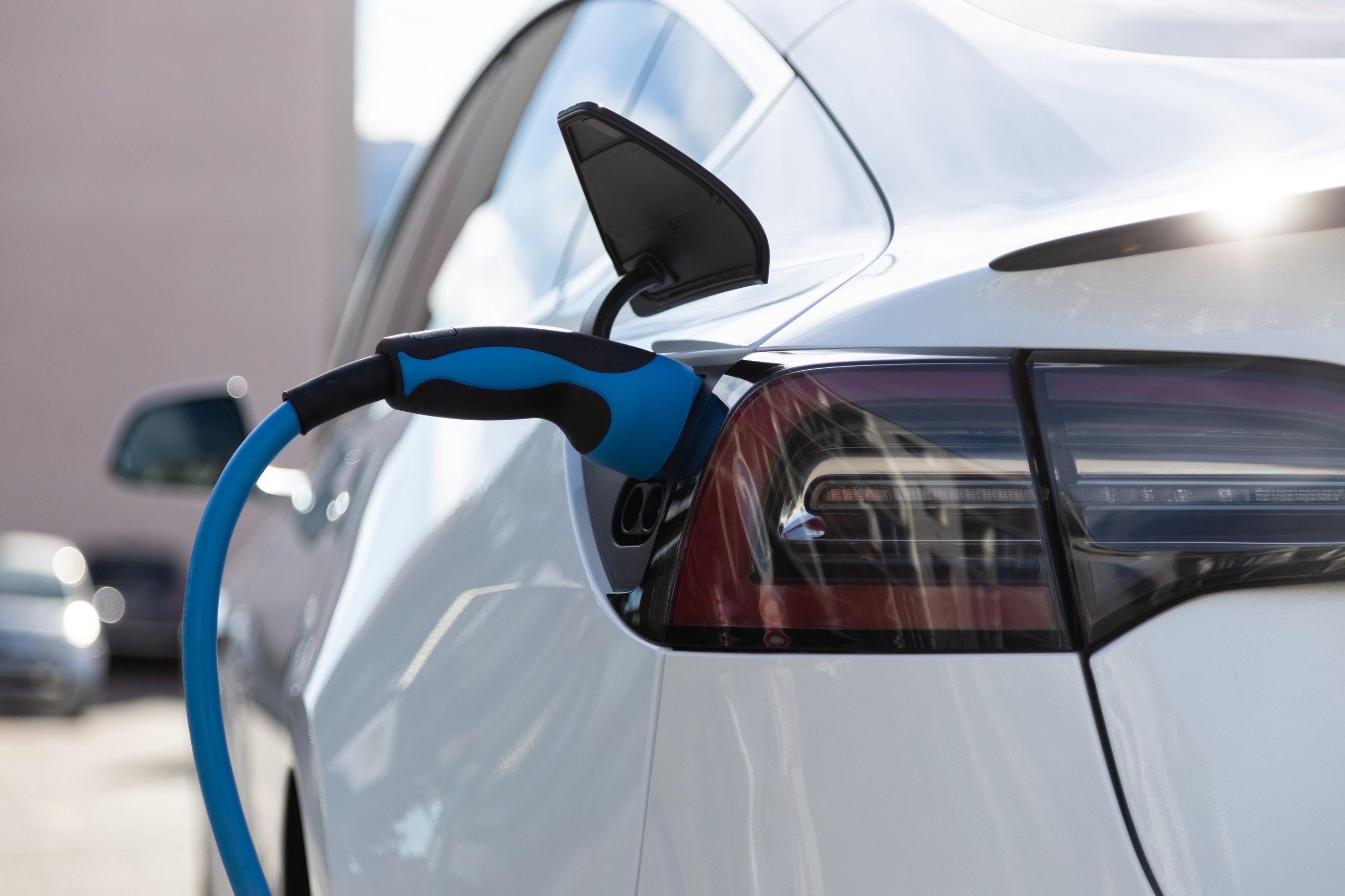 Close-up of a blue charging cable plugged into the port of a white electric vehicle parked outdoors.